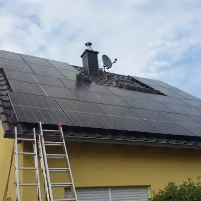 Gelbes Haus mit großer Solaranlage auf einem steilen Satteldach, inklusive Satellitenschüssel und Kamin.