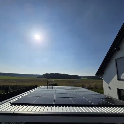 PV-Anlage auf einem flachen Blechdach, im Vordergrund offenes Feld und helle Sonne am Himmel. Komplette Photovoltaikanlage inkl. Montage und Anmeldung Solarfirma in der Nähe mit Montage und Anmeldung. Solarfirma in der Nähe Ihres Wohnorts