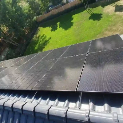 Flach montierte Solaranlage auf einem dunkelgrauen Ziegeldach, Blick von oben mit grünem Garten im Hintergrund.