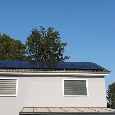 Flachdach mit grauem Putz und schmaler, horizontaler Solaranlage, Bäume im Hintergrund.