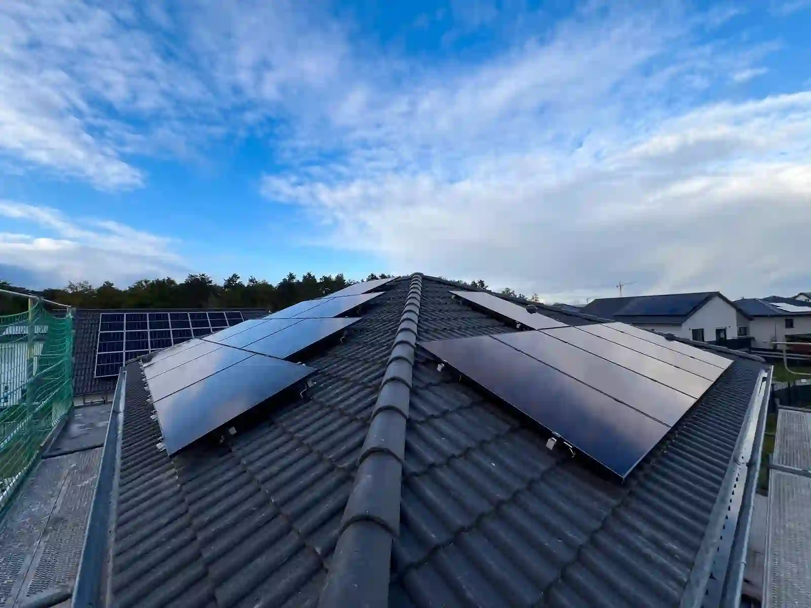 PV-Anlage auf beiden Seiten eines Satteldachs mit grauen Dachpfannen, Baustellengerüst und Nachbarhäuser sichtbar. Die Komplette Photovoltaikanlage inkl. Montage und Anmeldung