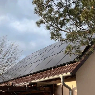 Schlichtes Haus mit braunem Ziegeldach, PV-Anlage im oberen Bereich, Baum ragt ins Bild