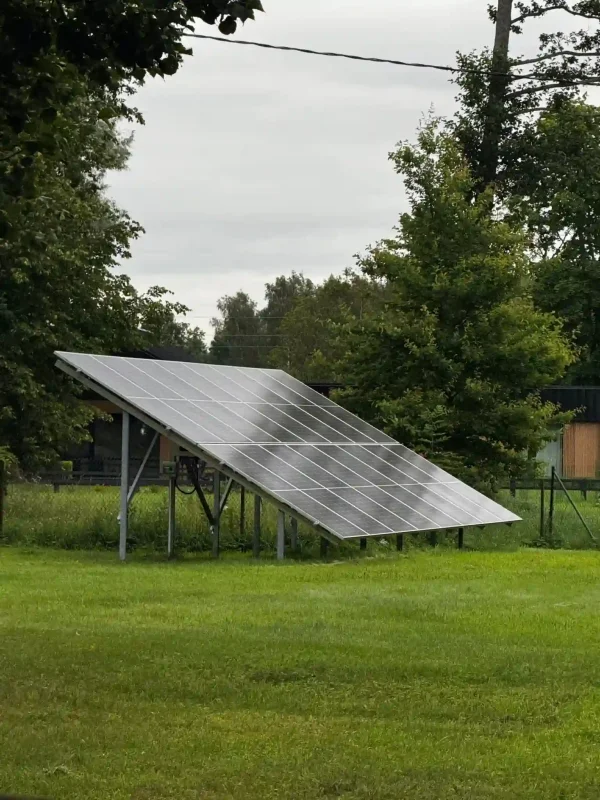 Auf dem Bild ist eine freistehende Solaranlage im Garten zu sehen. Die Photovoltaik-Module sind auf einem stabilen Metallgestell montiert und leicht geneigt, sodass sie möglichst viel Sonnenlicht aufnehmen können. Im Hintergrund erkennt man Bäume und eine grüne Wiese, was der Szene eine natürliche Umgebung verleiht.