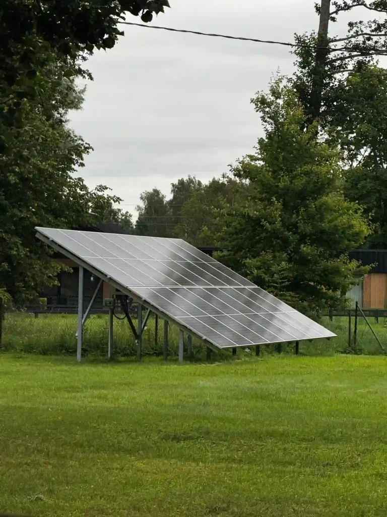 Auf dem Bild ist eine freistehende Solaranlage im Garten zu sehen. Die Photovoltaik-Module sind auf einem stabilen Metallgestell montiert und leicht geneigt, sodass sie möglichst viel Sonnenlicht aufnehmen können. Im Hintergrund erkennt man Bäume und eine grüne Wiese, was der Szene eine natürliche Umgebung verleiht.