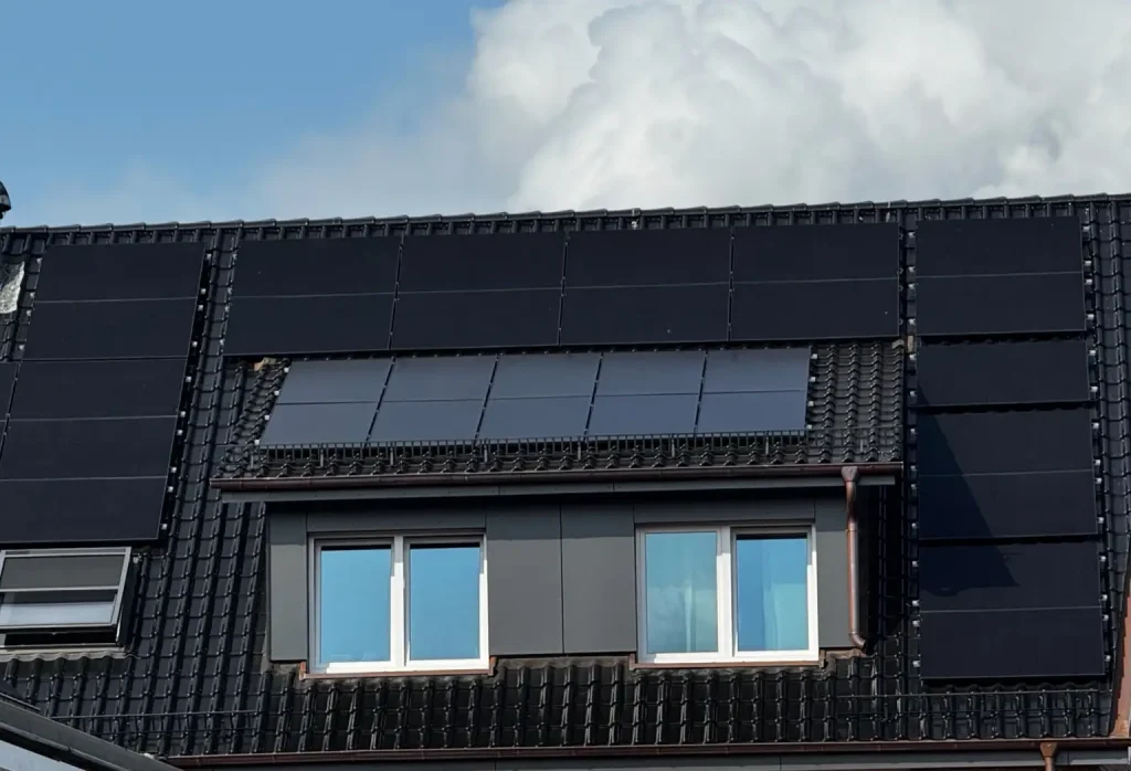 Das Bild zeigt die Dachfläche eines Hauses, die mit zahlreichen Photovoltaikmodulen ausgestattet ist. Die PV-Module sind gleichmäßig auf den dunklen Dachziegeln installiert und decken fast die gesamte Dachfläche ab. Besonders auffällig ist der PV Reinigungseffekt, da die Module durch ihre saubere Oberfläche gleichmäßig dunkel glänzen und so eine hohe Energieeffizienz gewährleisten. Saubere Solarmodule reflektieren weniger Schmutz und Staub, was den Stromertrag deutlich verbessert.