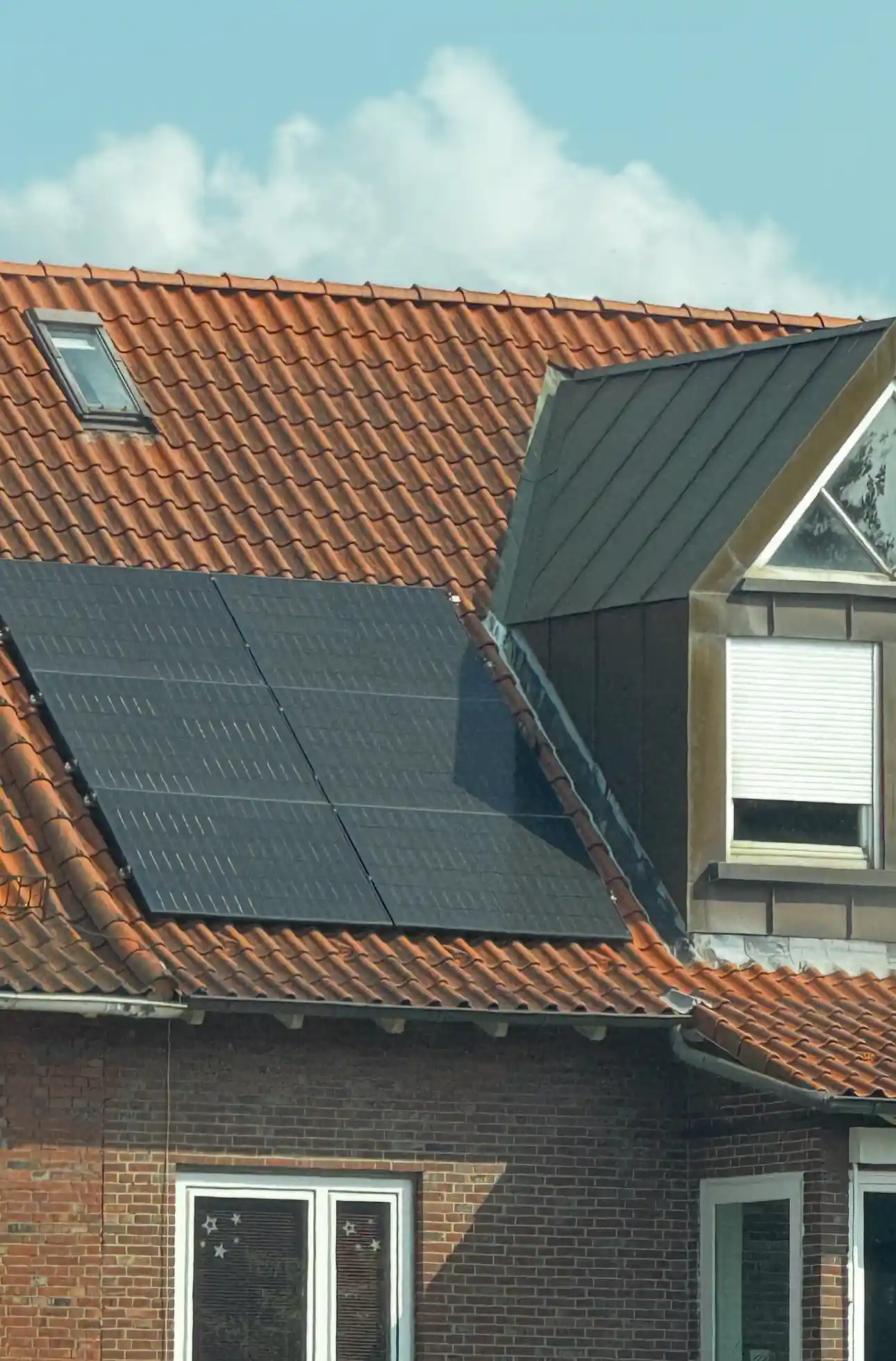 Auf dem roten Ziegeldach eines Wohnhauses sind mehrere Photovoltaik-Module installiert. Sie erzeugen Solarstrom, der sich optimal mit einem dynamische stromtarif kombinieren lässt, um Eigenverbrauch und Speicher effizient zu nutzen